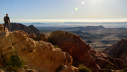 A man stands on a rock, gazing out over a vast, scenic valley below him.