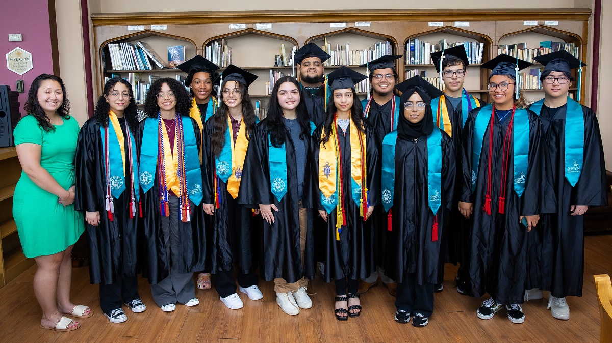 Horizontal image of 13 people that includes 12 high school seniors from Bayonne High School who earned an Associate Degree through the Early College Program and their Academic Counselor, Joycelyn Wong Castellano.