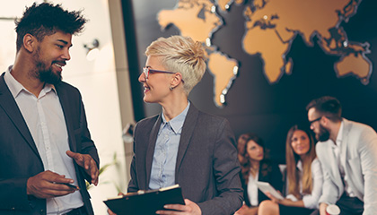 Two colleagues conversing, positioned in front of a large world map, symbolizing global business discussions.